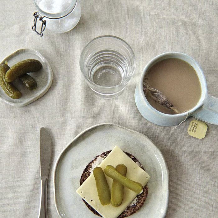 Ceramic plate and mug set with pickles and tea, styled on linen